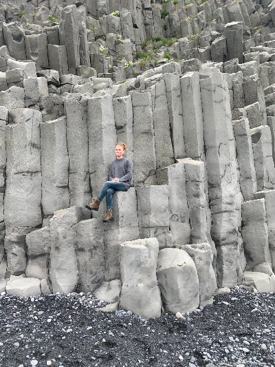 A woman sitting on some basalt stacks at Reynisfjara Black Sand Beach in Iceland