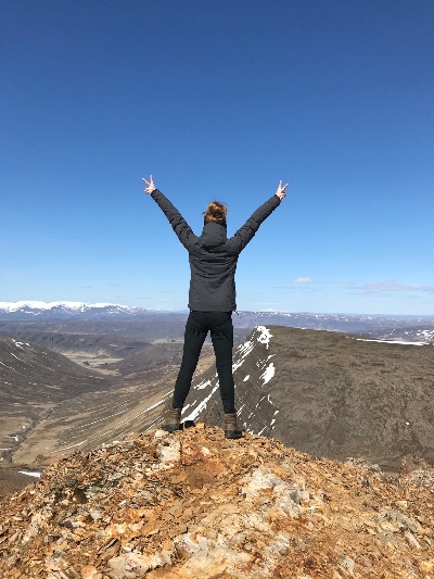 A hiker standing on the top of a rhyolite summit in Iceland with the back to the camera and both arms up in the air