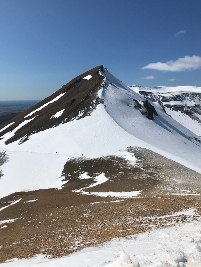 A hikers view over a partly snow covered summit and blue skies close to Reykjavík