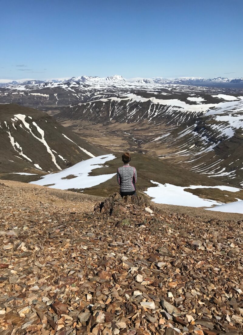 A hiker sitting on a rock on the top of Móskarðshnjúkar in Iceland