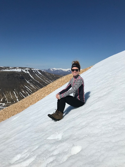 A hiker sitting in a pile of snow on her way up to the Móskarðshnjúkar summit