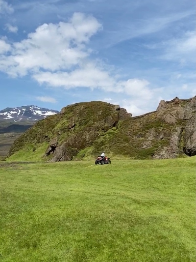 Green grass and mountains and a tiny ATV in the far