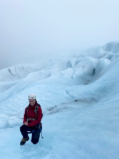 A hiker posing kneeling down on a glacier