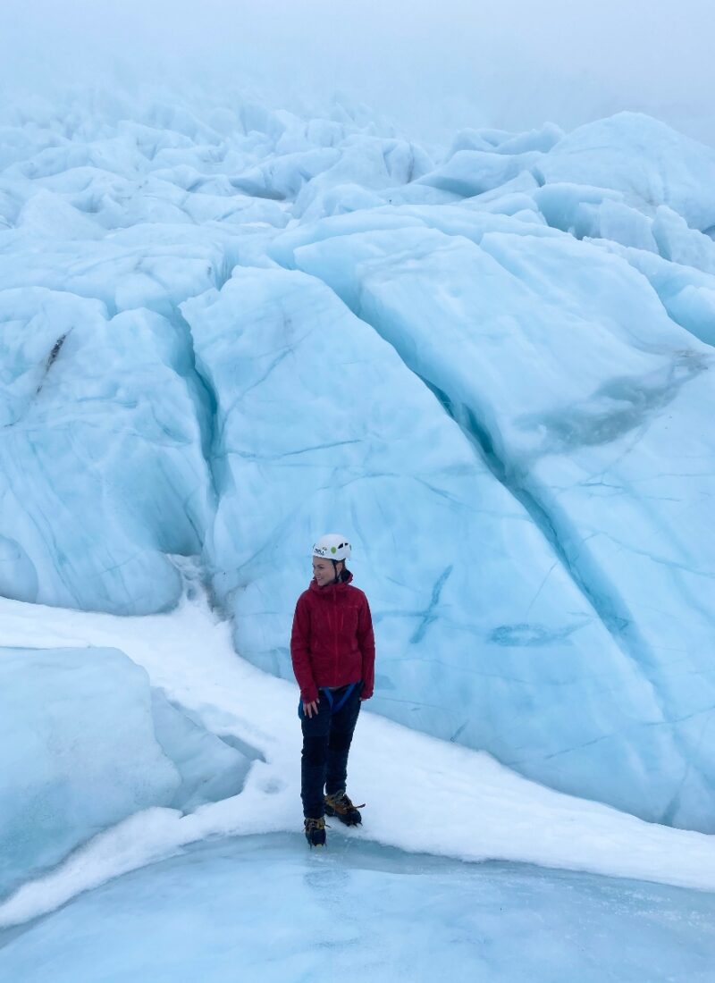 A hiker in a red jacket posing on a glacier