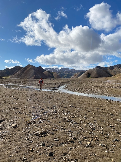 A hiker walking along brown sand in the Icelandic Highlands with mountains in the far 