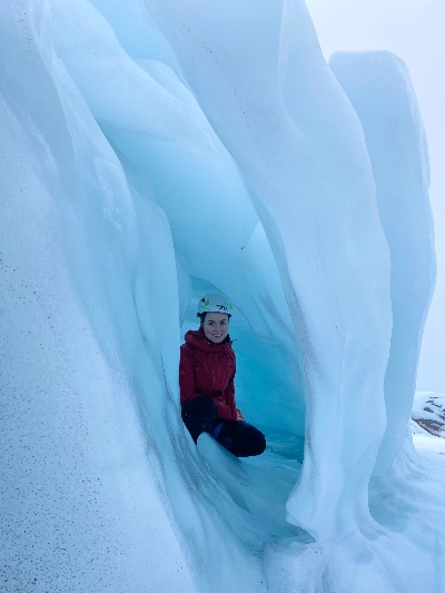 A hiker posing in a tiny ice cave or a sculpture on a glacier