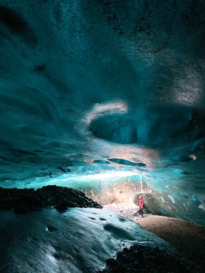 A person looking so tiny in a huge blue ice cave in Iceland