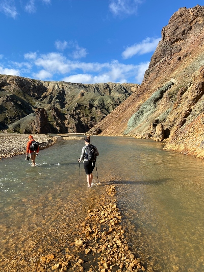 Hikers surrounded by rhyolite mountains wading a river