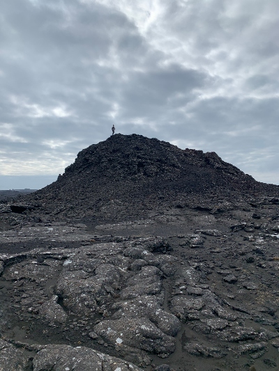  A hiker climbing on the top of a black volcanic crater, sourrounded by black lava on Reykjanes Peninsula in Iceland
