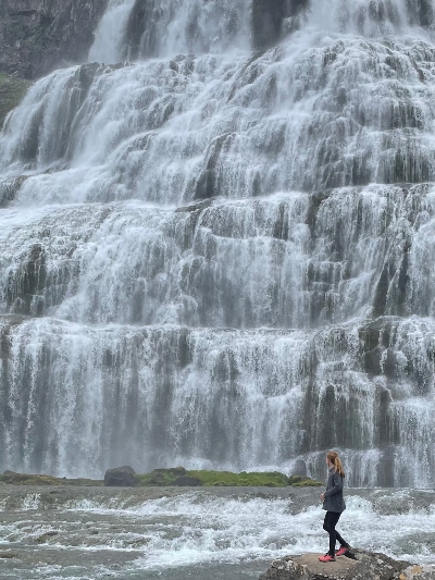 A woman looking so small standing close to the mighty Dynjandi Waterfall in Iceland