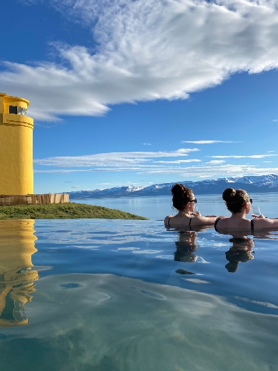 Two women admiring the mountain and ocean view on a beautiful day in Geosea geothermal bath in Iceland