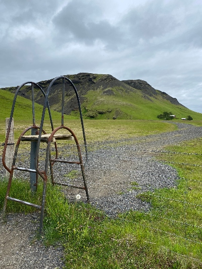 Small rusty stairs over a fence on a trail to Kvernufoss in Iceland with a mountain in the background