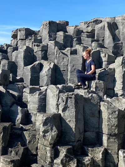 A woman in blue sitting on some basalt columns on a sunny day