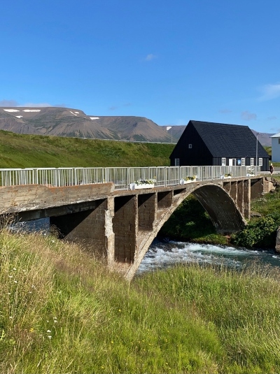 An old stone bridge with an old black house and mountains in the background