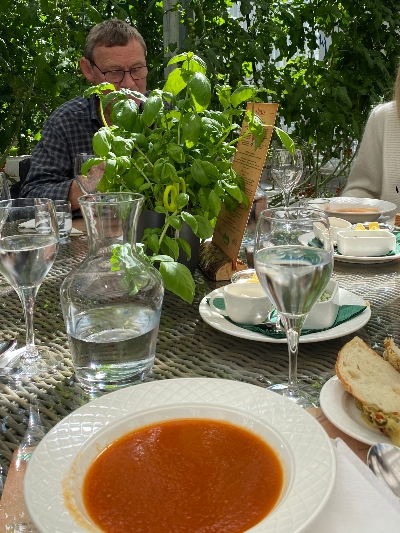 A plate with tomato soup on table with glass wear and a fresh basil plant at Friðheimar Tomato Farm