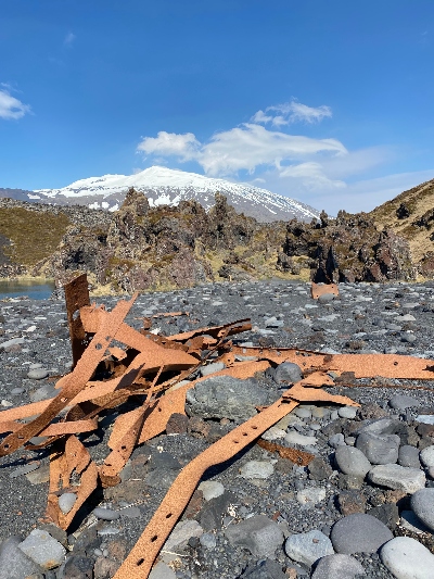 Rusty iron remains laying around on a black beach in Iceland with Snæfellsjökull glacier in the background
