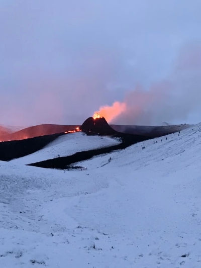 An Icelandic volcano in action seen from afar surrounded by snowy ground