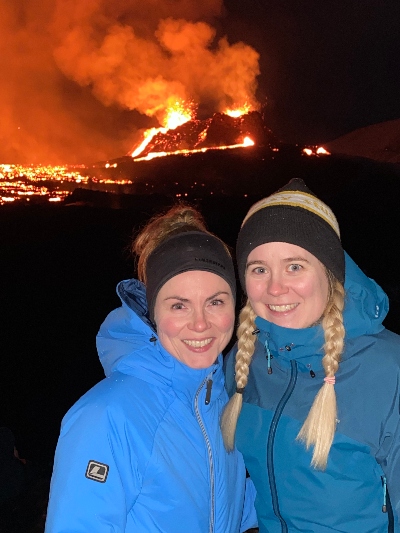 Two smiling hiker girlfriends posing in front of an active volcano in the dark