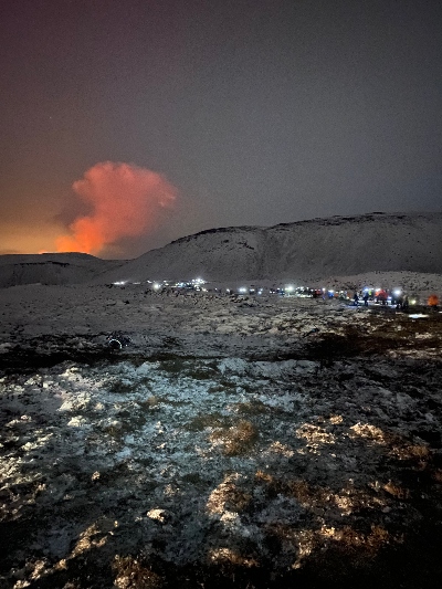 Many hikers with head lights hiking towards an active volcanic eruption in the dark