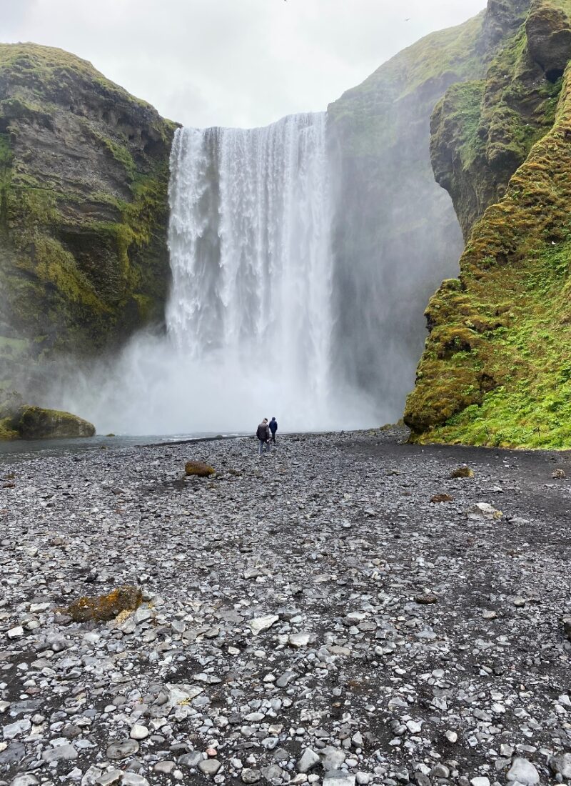 Two people walking towards Skógafoss Waterfall in Iceland