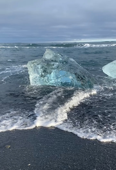 A chunk of ice that looks like a big diamond on a black sand beach