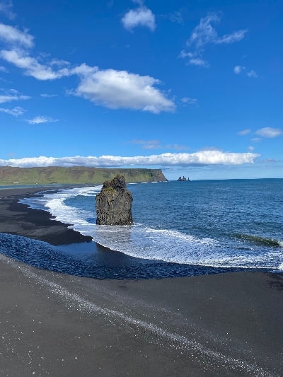 A huge sea stack standing alone on a black sand beach close to Dyrhólaey Iceland