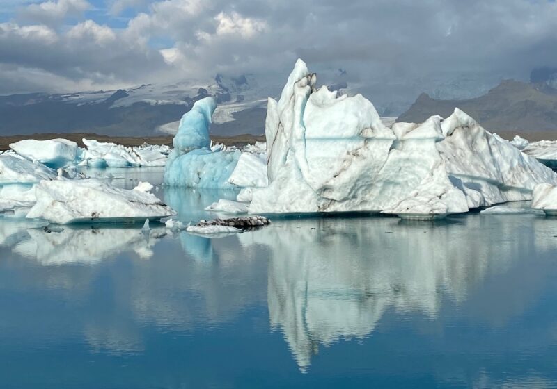 Blue and white icebergs with black stripes in them floating around on a blue lagoon