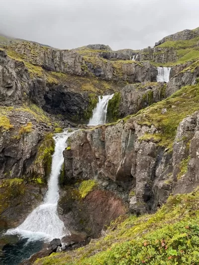 A numerous small waterfalls falling down a rocky hill in East Iceland