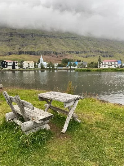 A table and a bench made of driftwood by the lagoon in Seyðisfjörður with a few old houses in the background