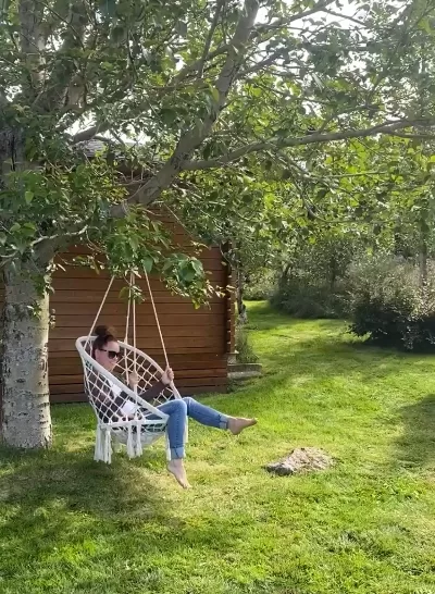 A woman sitting in a cozy swing attached to a leafy tree