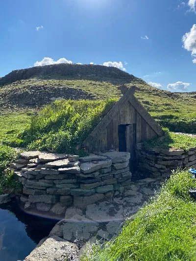 A small cute old looking shed with a grass roof next to a hot spring called Hrunalaug in Iceland