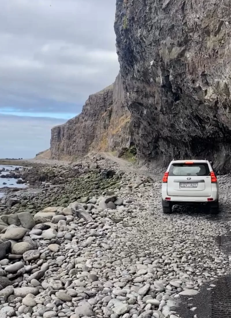 White big jeep driving on a rough gravel road with cliffs hanging over it.